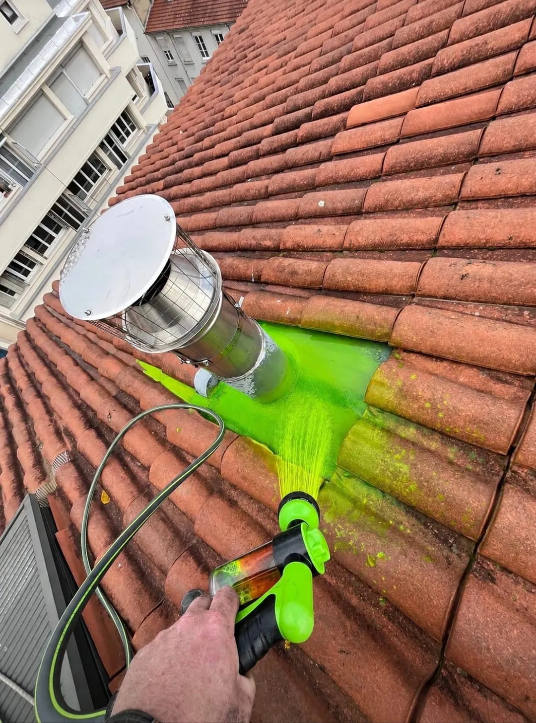Test d’aspersion avec eau colorée verte sur une toiture en tuiles autour d’une sortie métallique