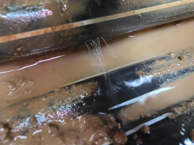 Fuite d'eau visible sur une canalisation enterrée dans une fouille boueuse