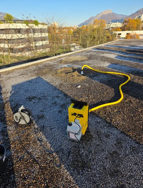 Générateur de fumée jaune raccordé à un tuyau sur une toiture-terrasse gravillonnée