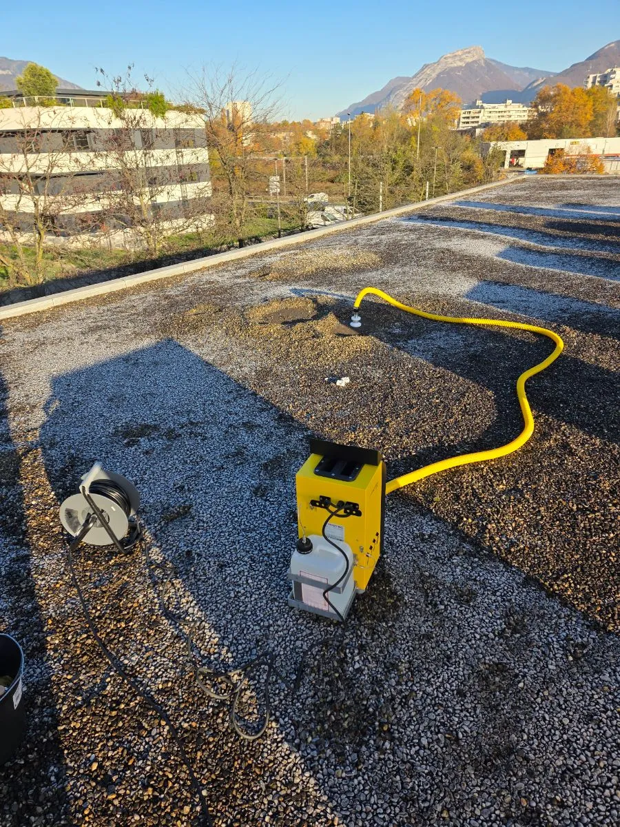 Générateur de fumée jaune raccordé à un tuyau sur une toiture-terrasse gravillonnée